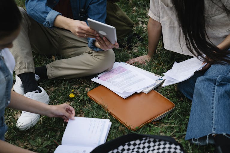 A group of students studying together outside, using a tablet and papers on the grass.