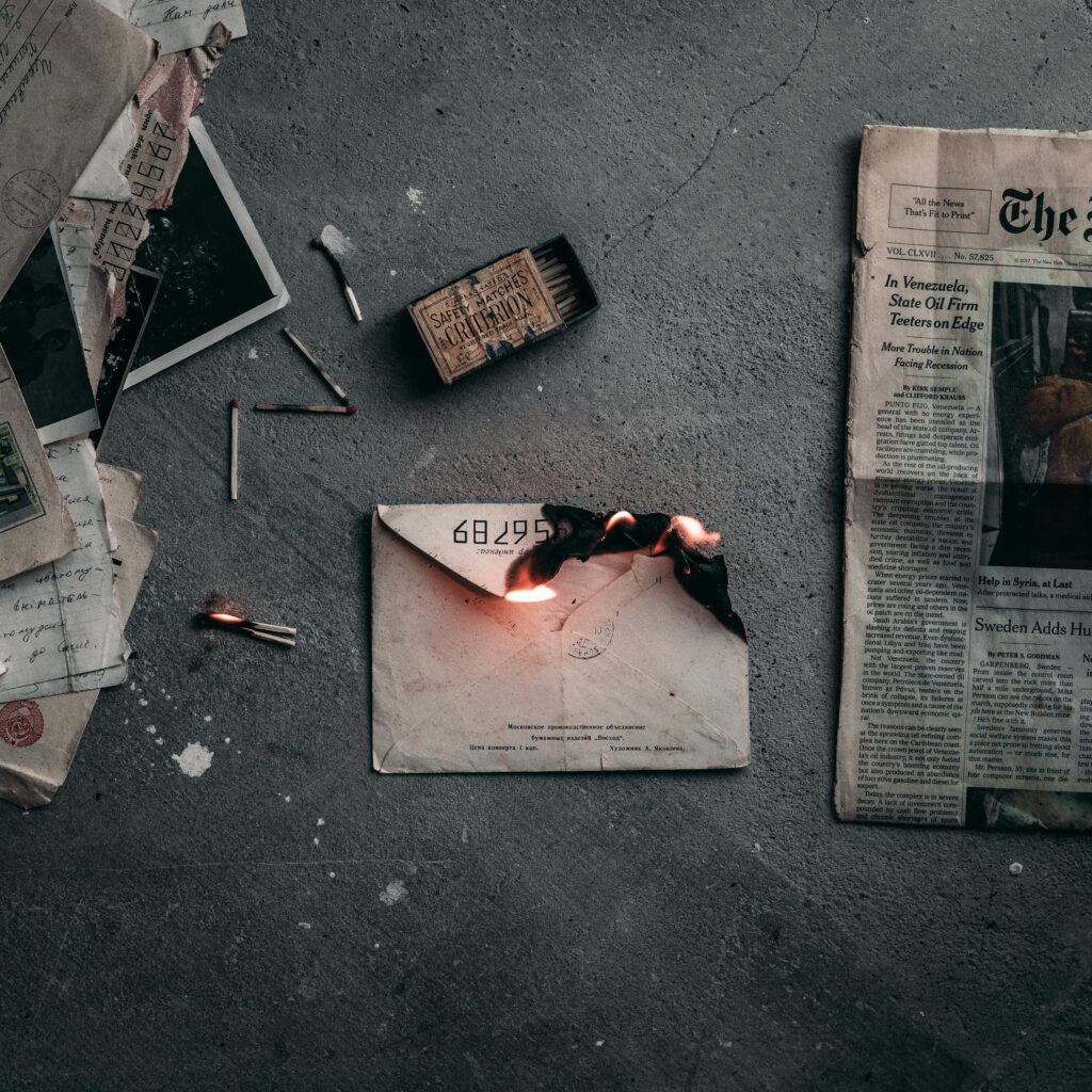 letter writing therapy - a dramatic scene of a burning envelope surrounded by matchsticks and old papers on a concrete floor.