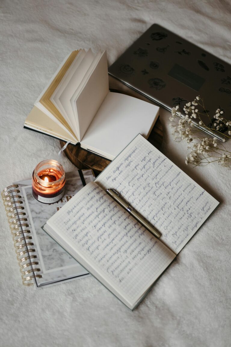 A serene writing setup featuring notebooks, a lit candle, and a laptop in a cozy indoor setting suggesting the best journals for healing.