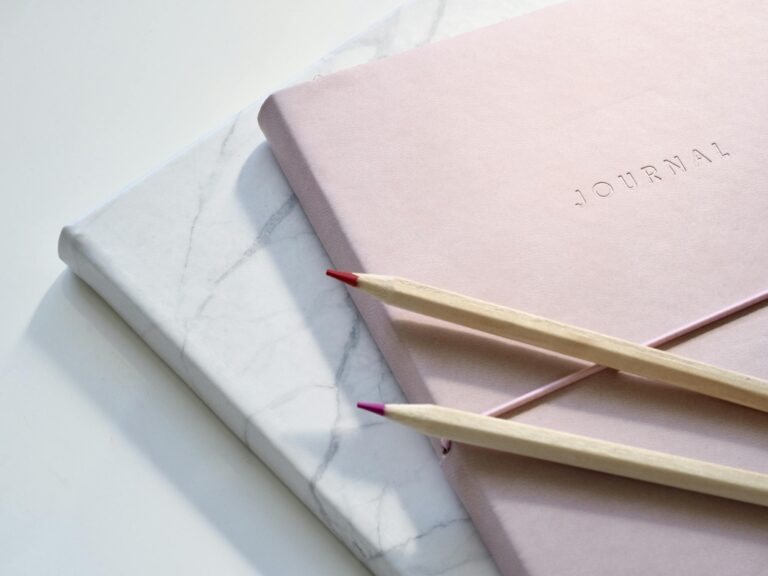 Close-up of a pink journal with pencils on a marble top to disprove journaling myths.