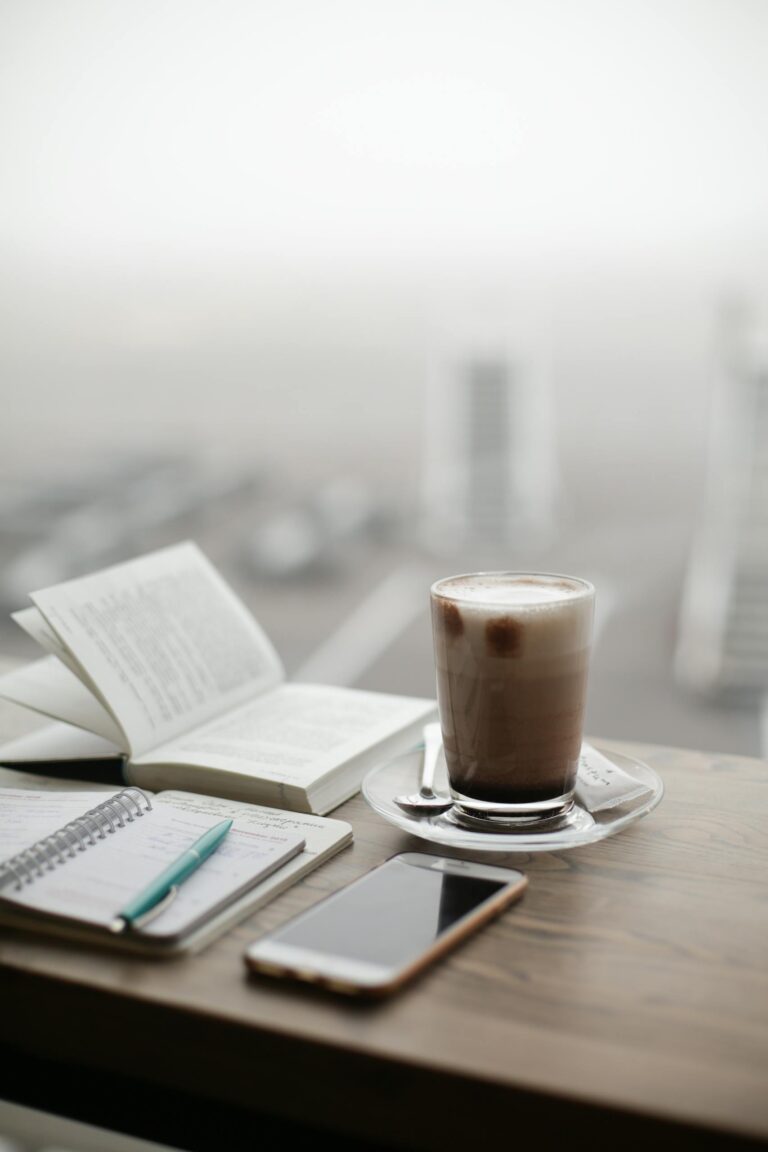 journaling prompts for beginners - a warm coffee sits beside a notebook and smartphone on a foggy day.