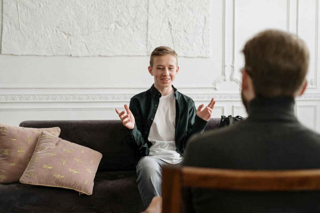 Nonviolent communication - Teen in discussion with therapist on a sofa during a counseling session indoors.